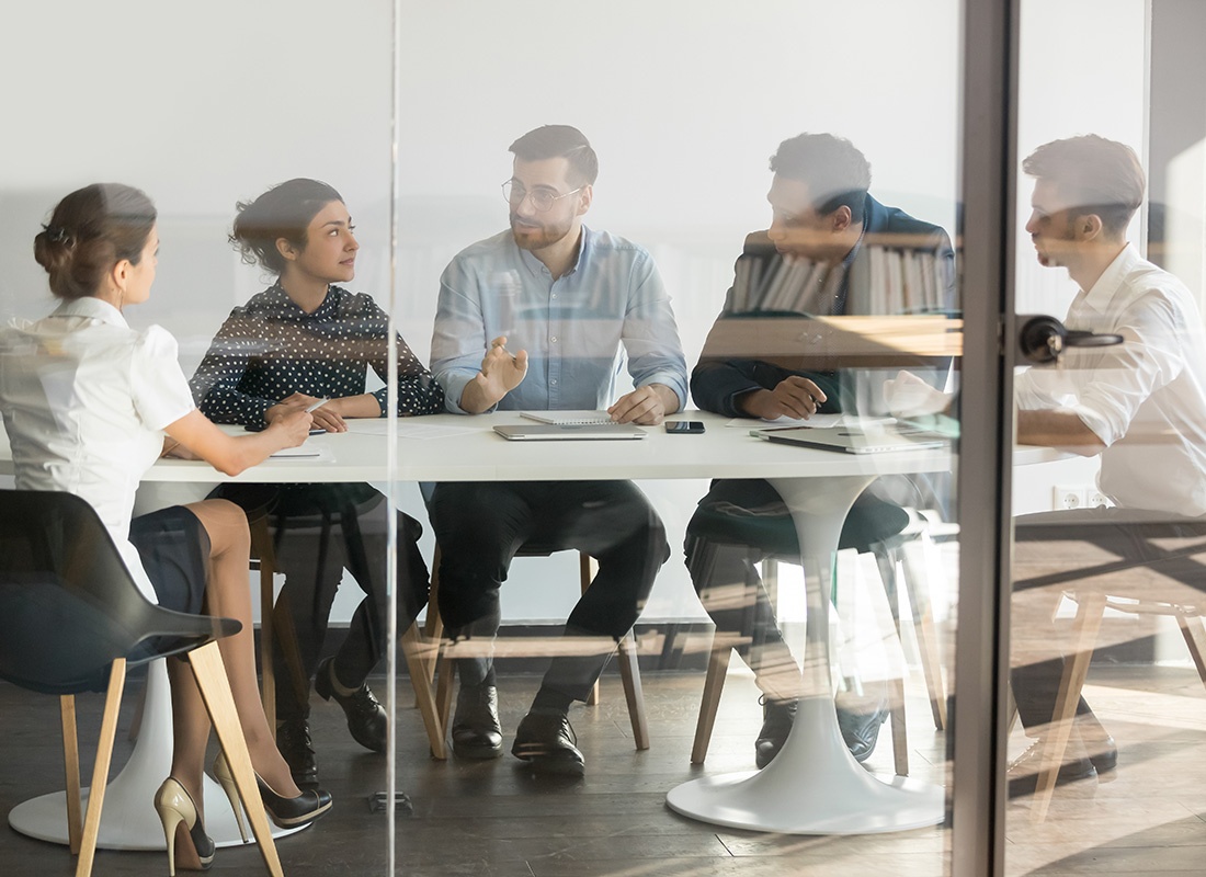 About Our Agency - Looking Through the Glass at a Small Group of Business People Communicating During a Meeting in a Modern Office