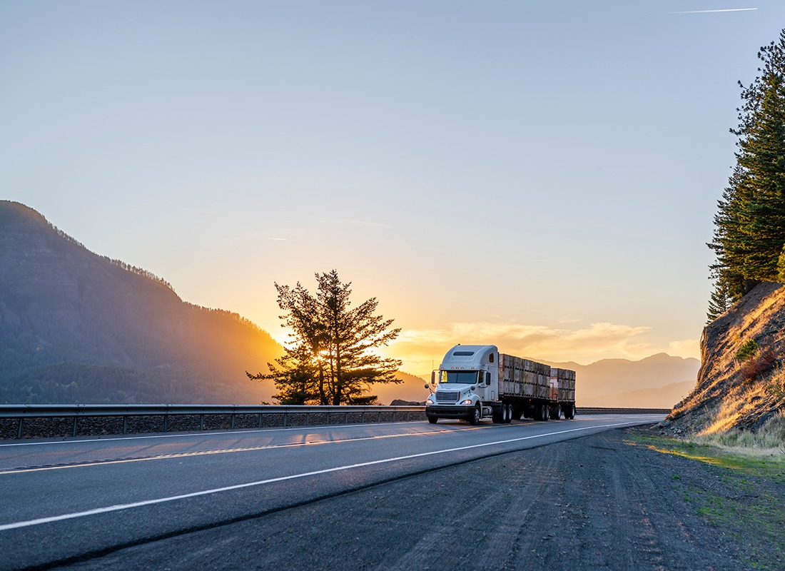 Business Insurance - View of a Tractor Trailer Truck Pulling Cargo on an Empty Highway with a Scenic View of the Mountains and Sunset in the Background