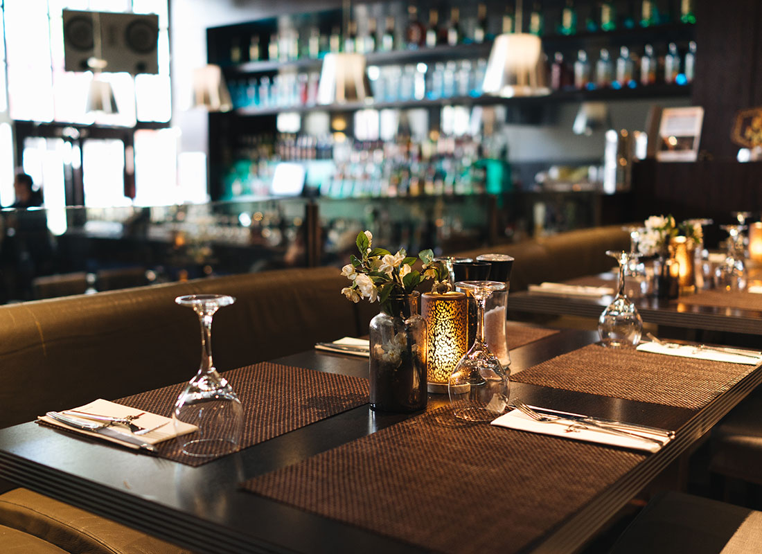 Insurance by Industry - View of Tables with Glasses Napkins and Candles Inside a Modern Restaurant with the Bar Area Visible in the Background